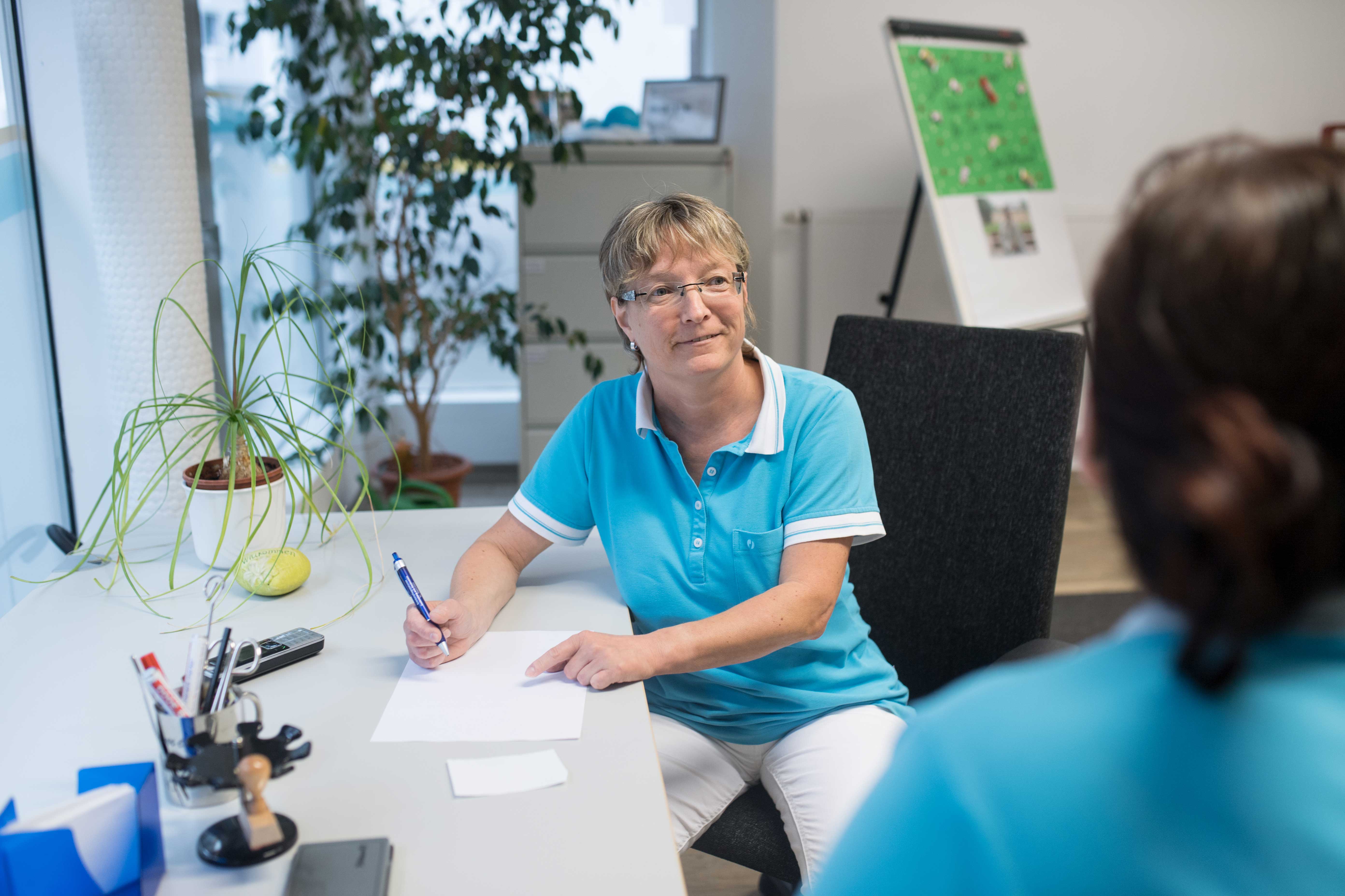 Eine Mitarbeiterin am Schreibtisch und eine Mitarbeiterin steht davor